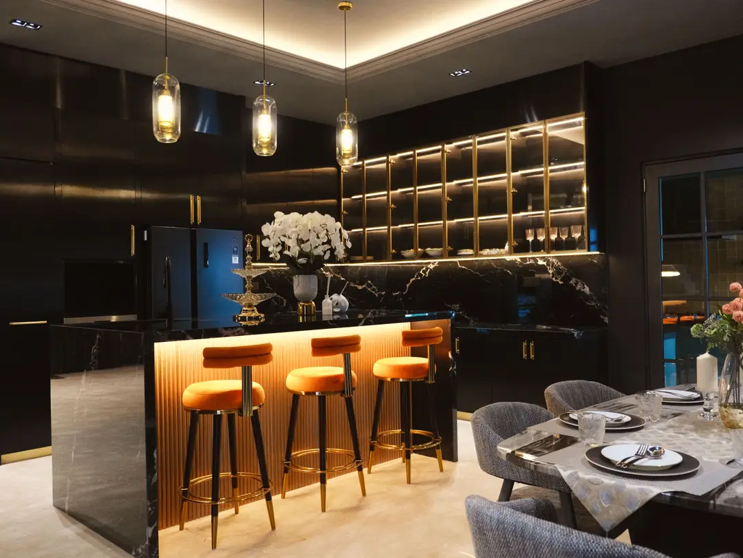 Black marble kitchen island with orange bar stools and gold-framed glass cabinets