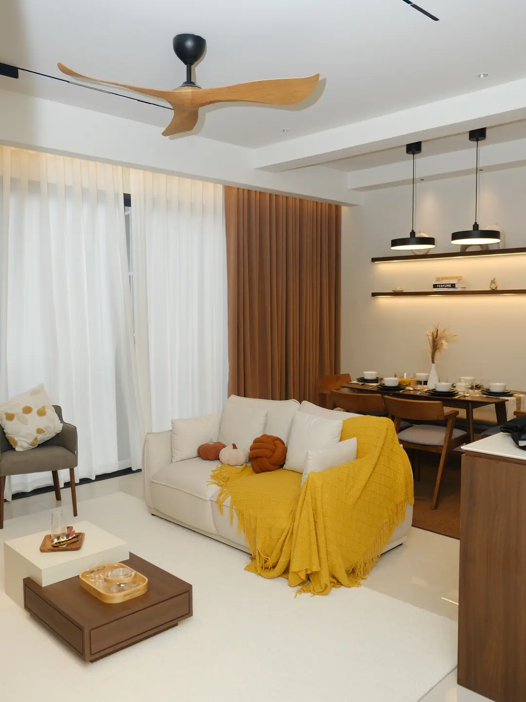 Bright condo living room with cream sofa, timber dining area and warm wood shelving